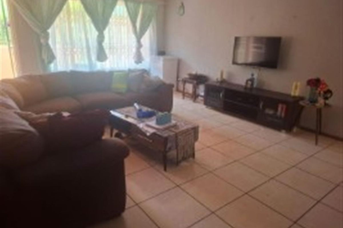 A spacious living room featuring neutral ceramic floor tiles and large windows with natural light, providing a comfortable and functional living area.