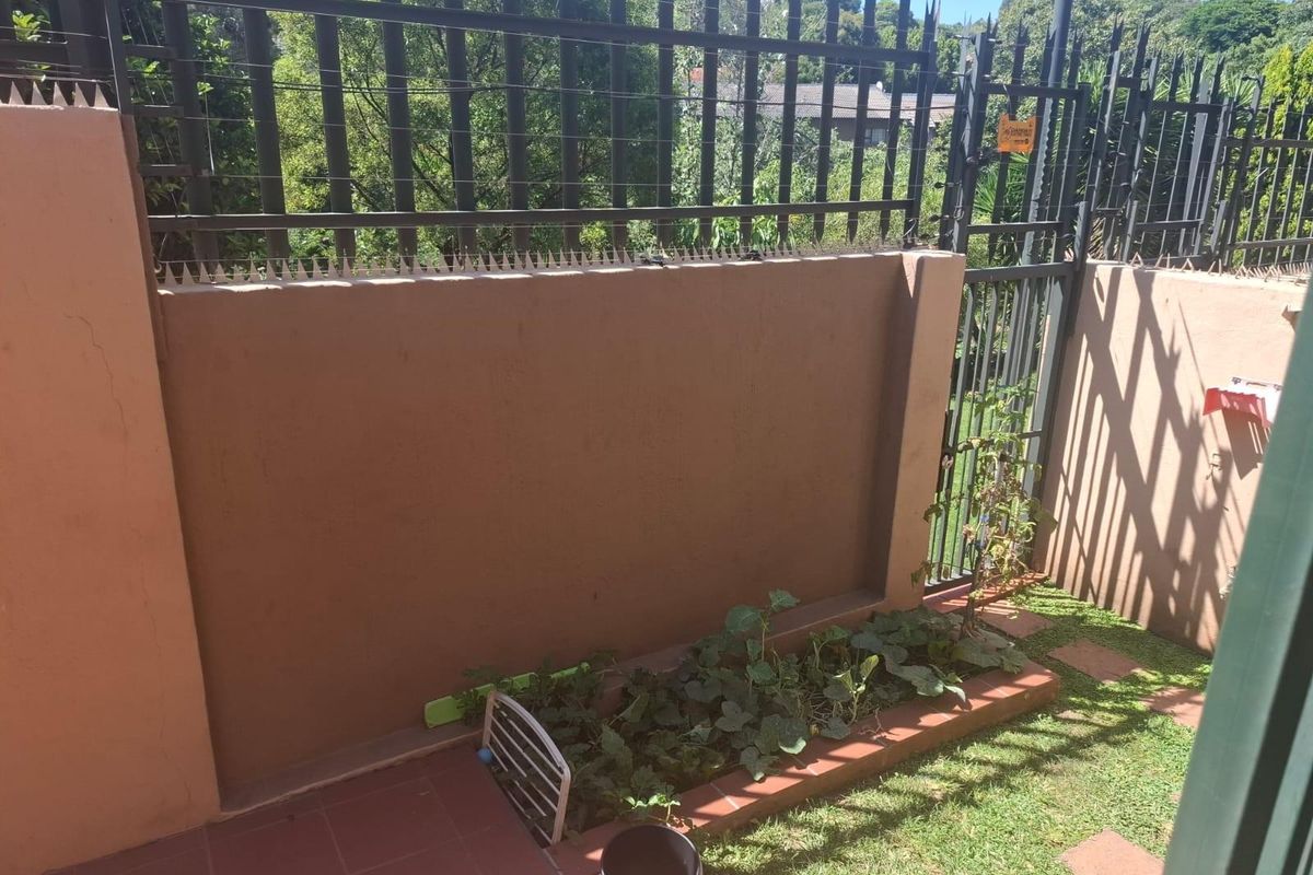 A private rear garden area featuring a paved patio, a small raised garden bed, and secure perimeter fencing with integrated security spikes.