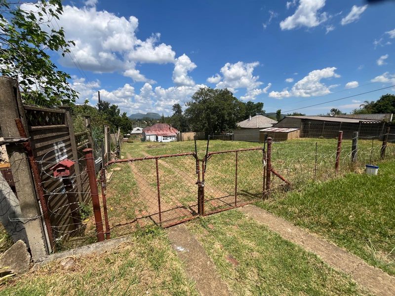 A view of a large, undeveloped plot of land featuring basic chain-link perimeter fencing and a metal gate entrance.