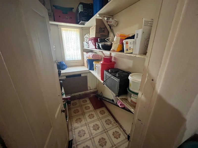 A compact scullery or pantry area featuring built-in shelving, vinyl flooring, and a small window for natural light.