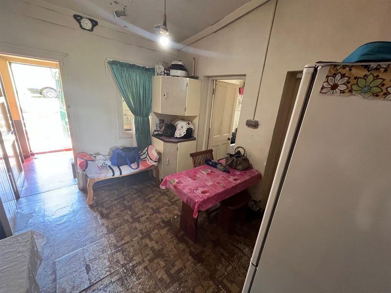 A compact, dated kitchen area featuring original cabinetry, tiled flooring, and direct access to the exterior, requiring significant cosmetic updates and maintenance.
