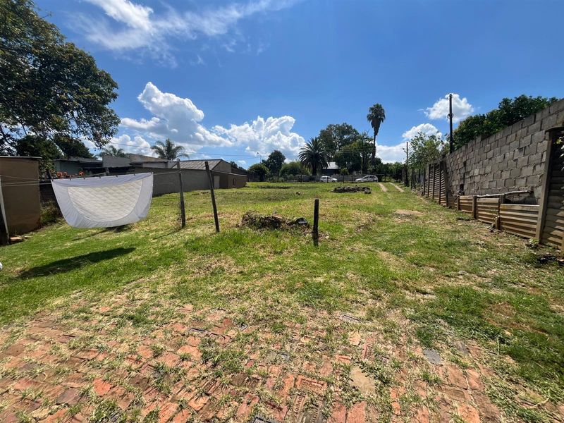 A spacious, undeveloped backyard area featuring a brick-paved section, grass lawn, and perimeter boundary walls.