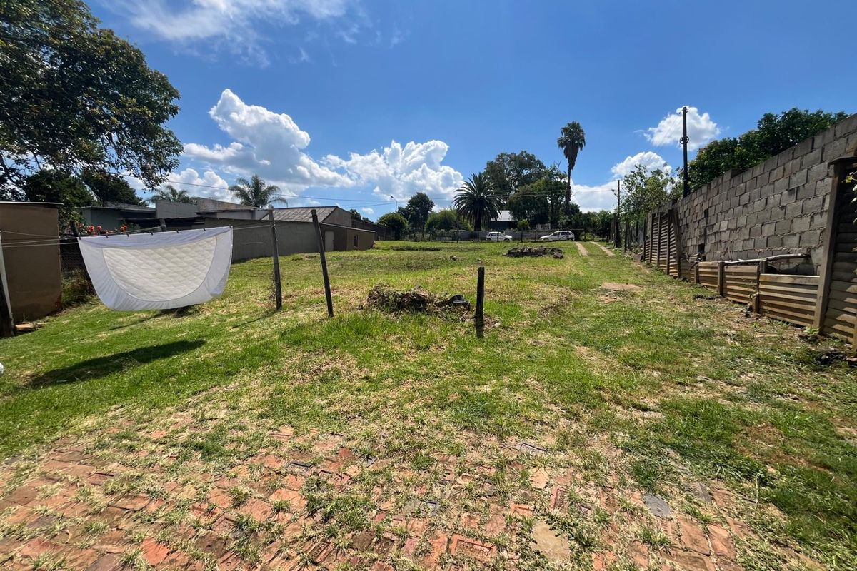 A spacious, undeveloped backyard area featuring a brick-paved section, grass lawn, and perimeter boundary walls.