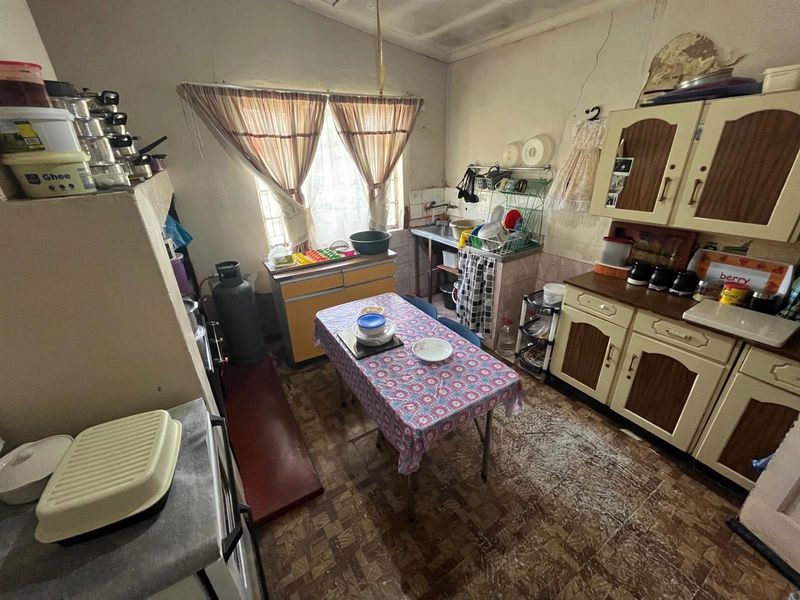 A dated kitchen area featuring original cabinetry, a small dining space, and a window, requiring significant renovation and modernization of finishes.