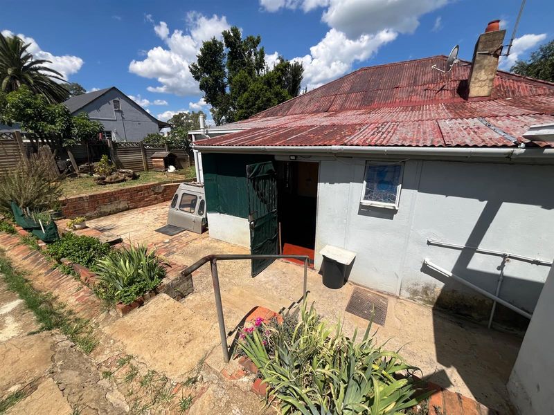Rear exterior view of the property featuring a corrugated metal roof, concrete patio area, and brick retaining wall elements.