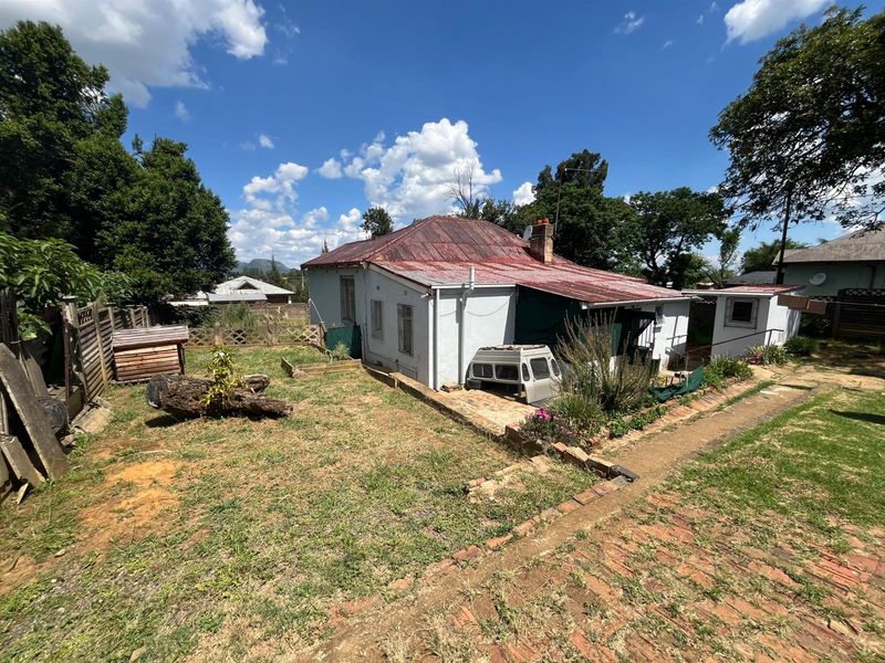 Rear view of a detached house featuring a corrugated metal roof, brick pathway, and a spacious garden area with established trees.