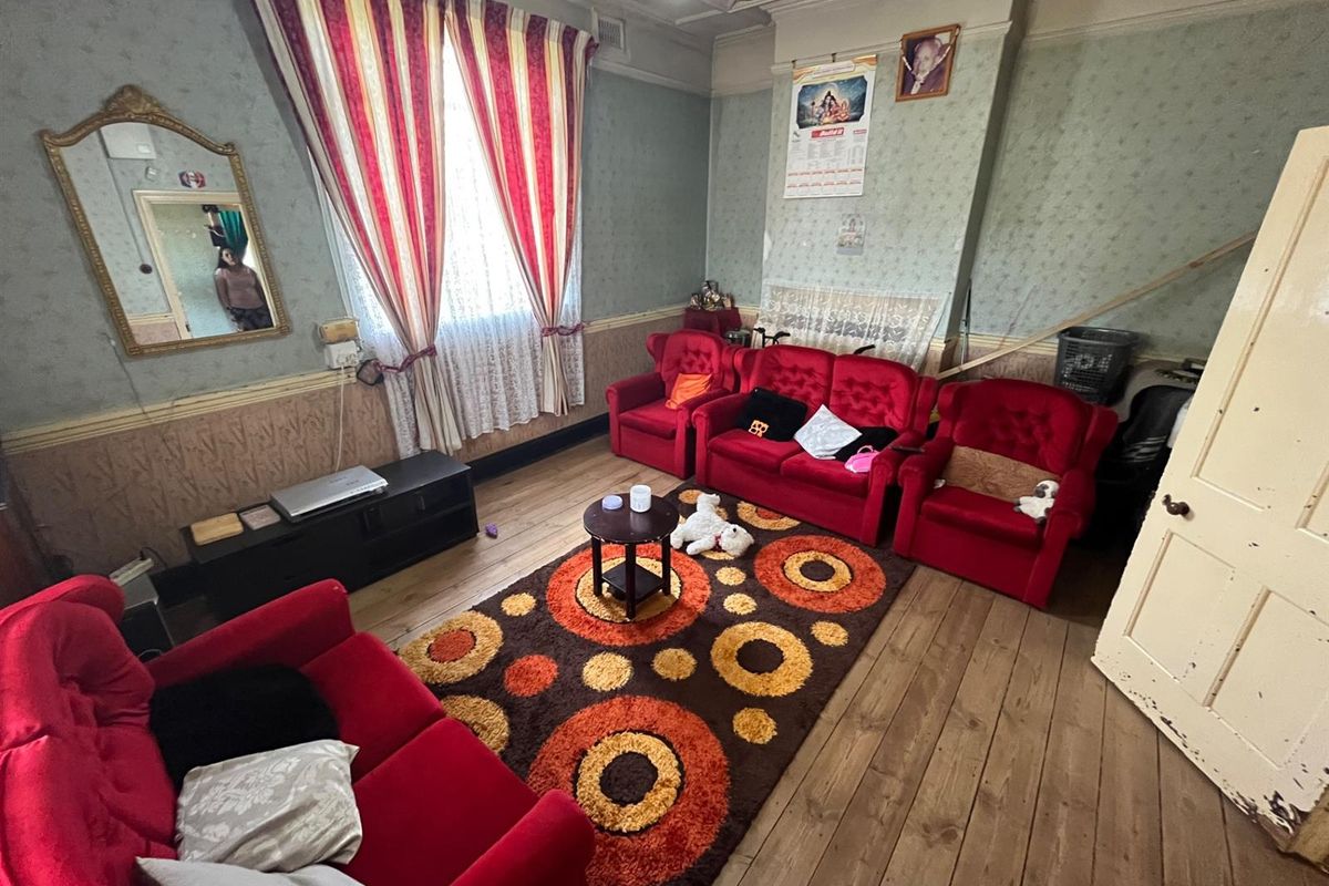 A traditional living room featuring timber flooring, decorative wall panelling, and a classic layout with ample natural light from the window.