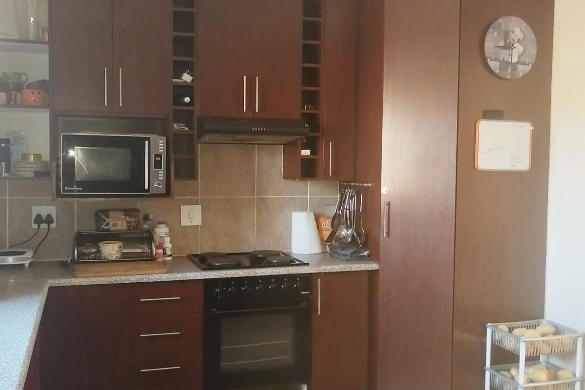A functional kitchen featuring dark wood cabinetry, built-in oven, hob, extractor fan, and tiled splashbacks with ample storage space.