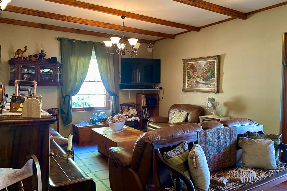 A cozy living room featuring exposed timber ceiling beams, terracotta floor tiles, and a classic chandelier, creating a warm and traditional atmosphere.