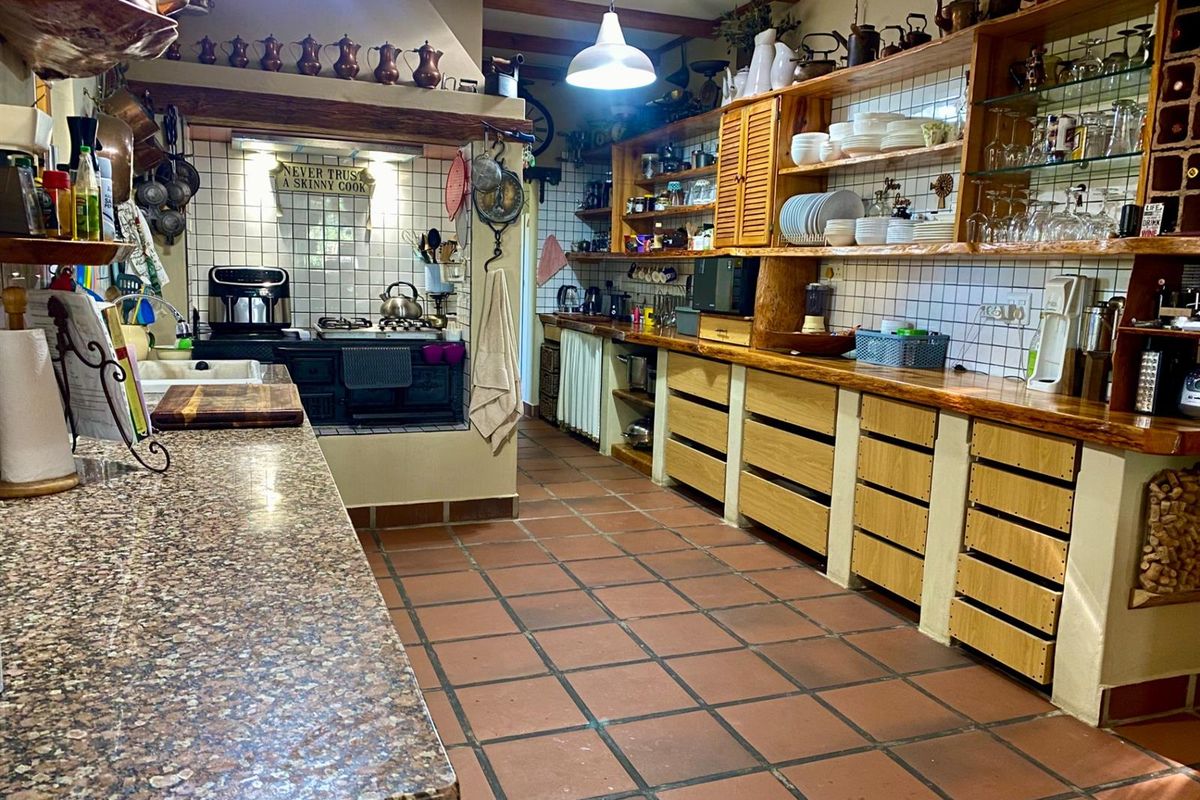 Rustic kitchen featuring granite countertops, tiled flooring, exposed timber ceiling beams, and extensive open shelving with built-in cabinetry.