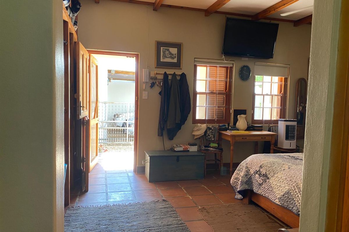 A bedroom featuring exposed timber ceiling beams, terracotta floor tiles, and direct access to an outdoor area through a wooden door.