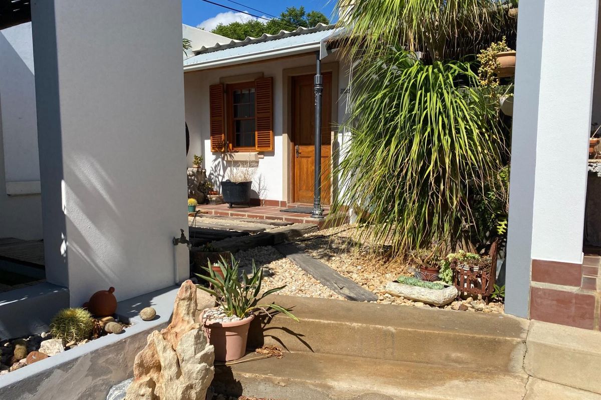 A charming exterior view of a cottage-style entrance featuring a wooden door, timber shutters, and a landscaped garden path.