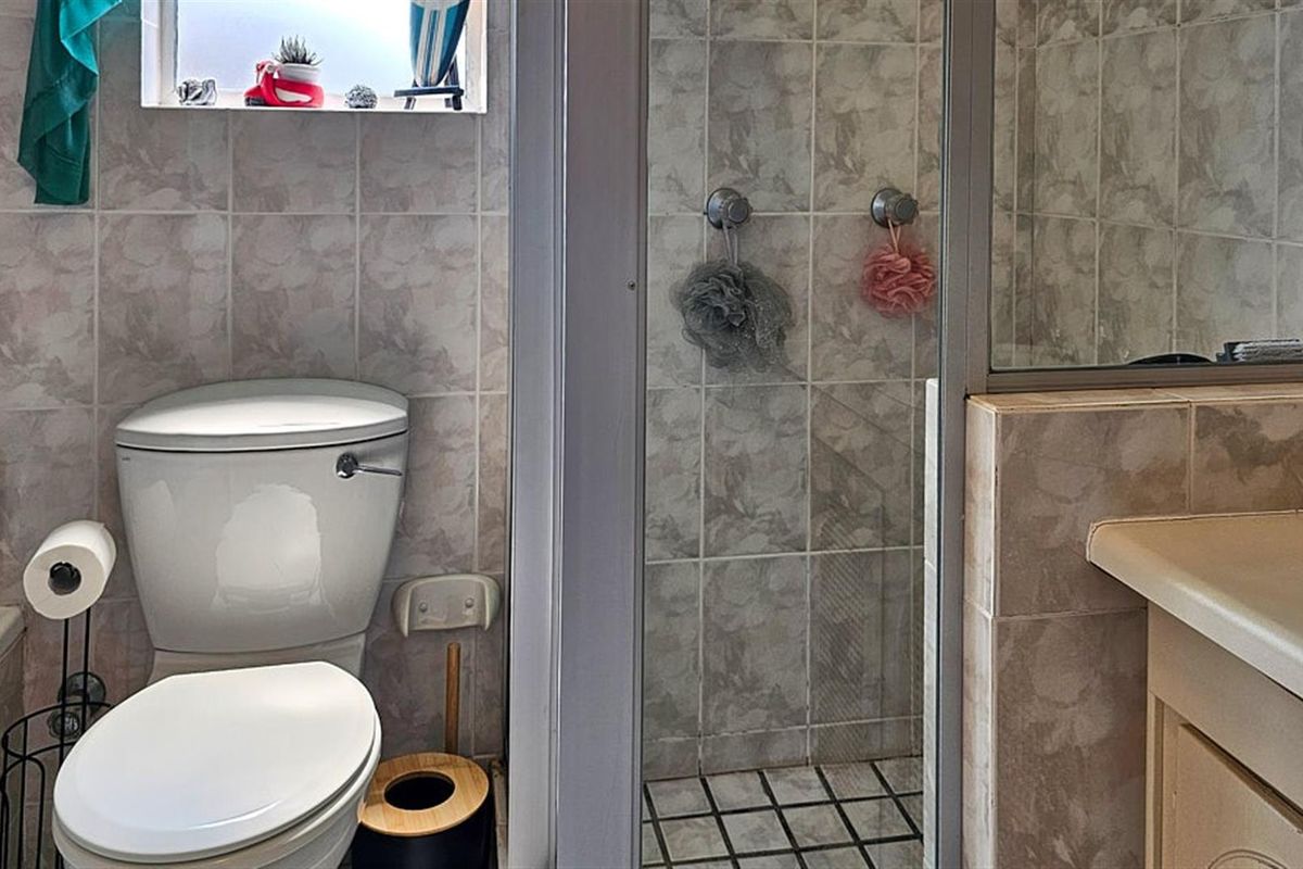 A functional bathroom featuring a toilet, a tiled shower enclosure, and a vanity unit with a basin.