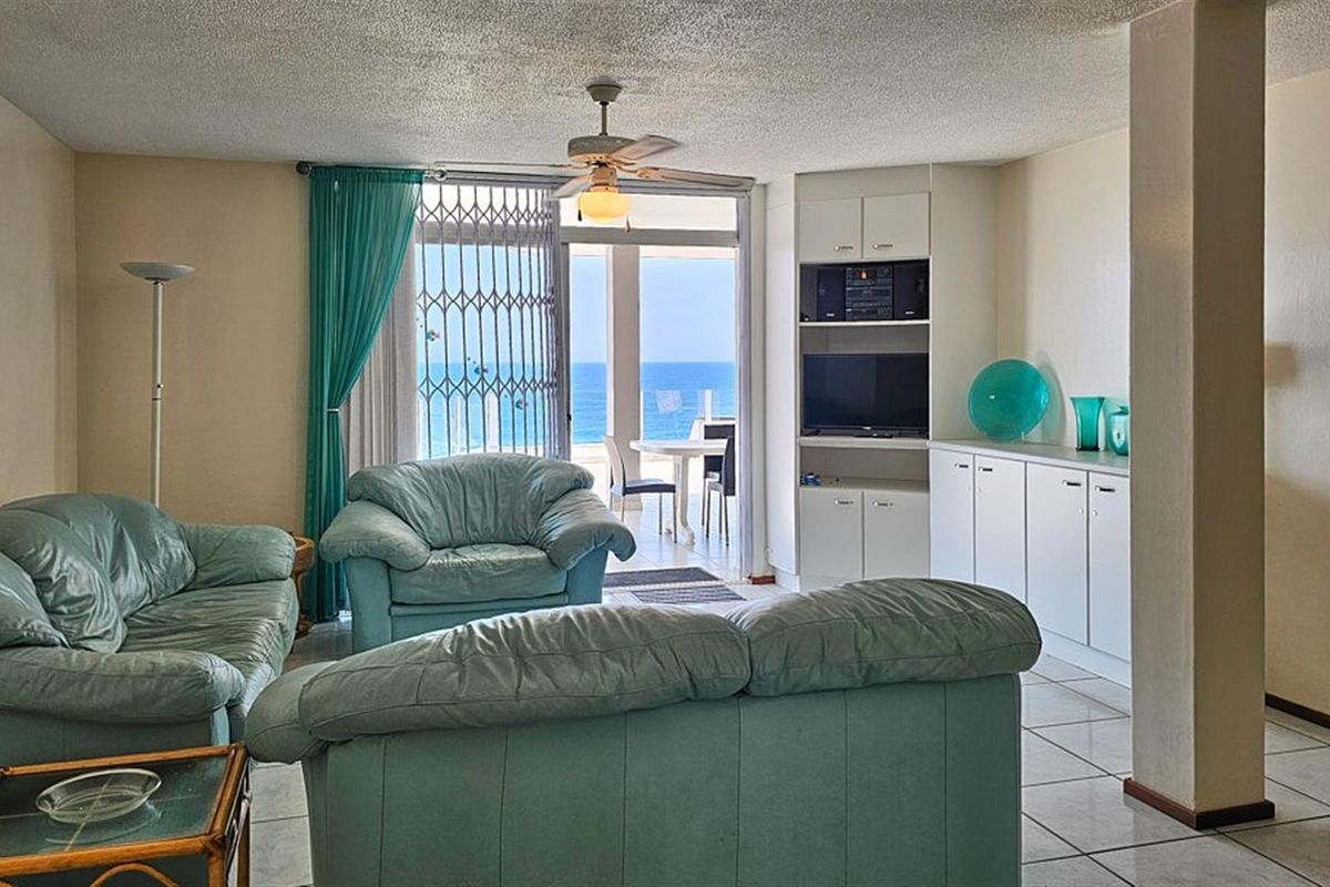 Spacious living area featuring built-in cabinetry, tiled flooring, and a ceiling fan, with direct access to a balcony offering scenic ocean views.