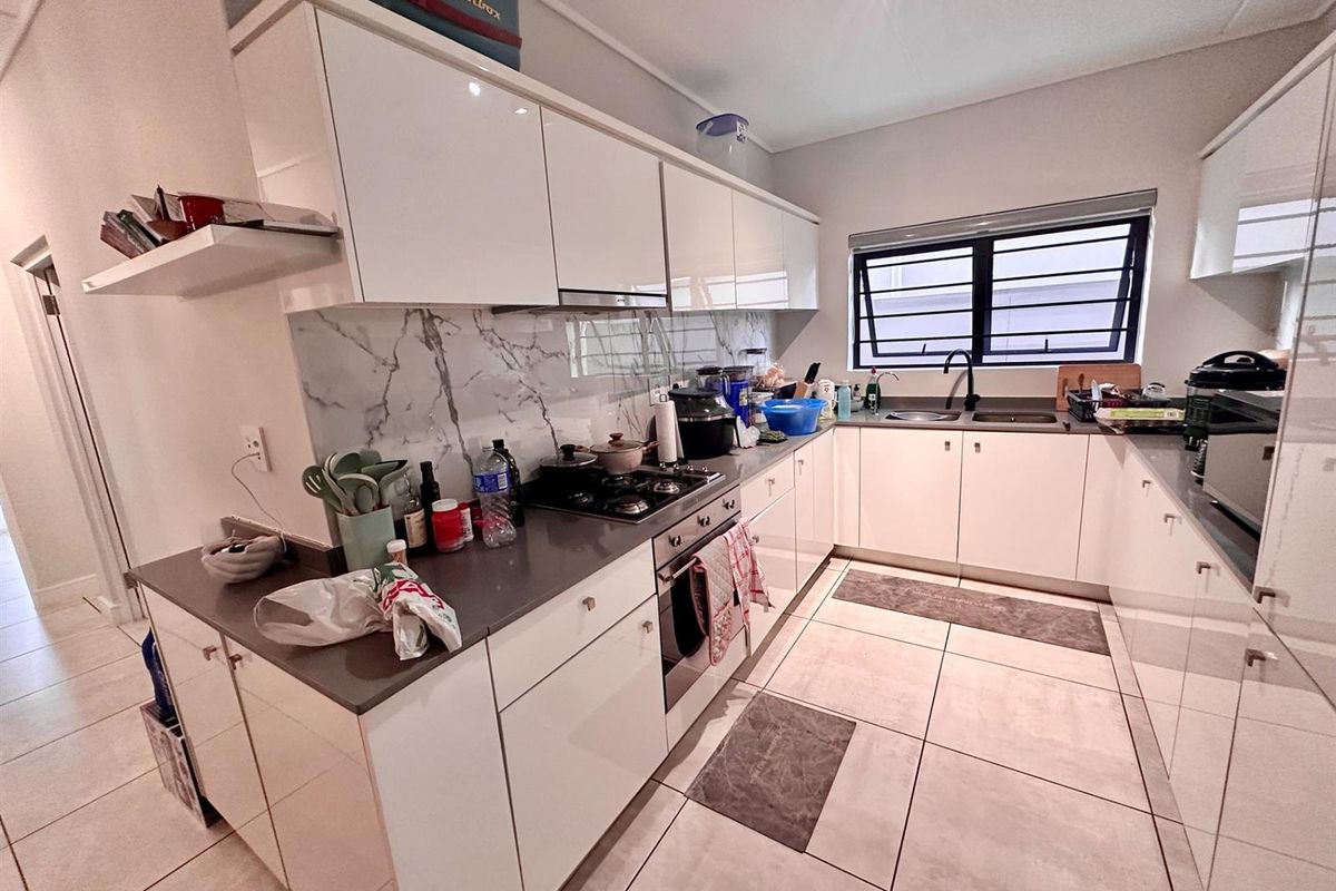 Modern kitchen featuring white high-gloss cabinetry, stone countertops, marble-look splashback, built-in oven, gas hob, and tiled flooring.