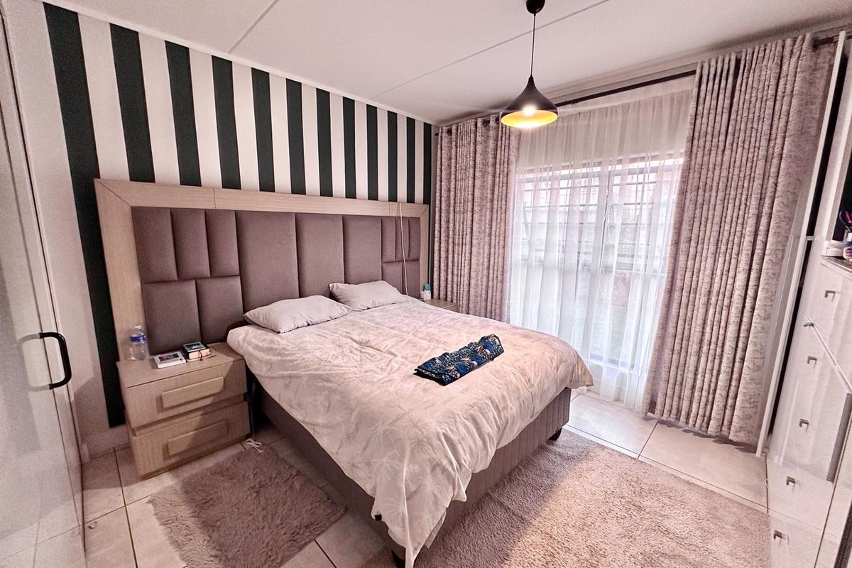 A well-maintained bedroom featuring tiled flooring, a built-in headboard, and large windows with floor-to-ceiling curtains providing ample natural light.