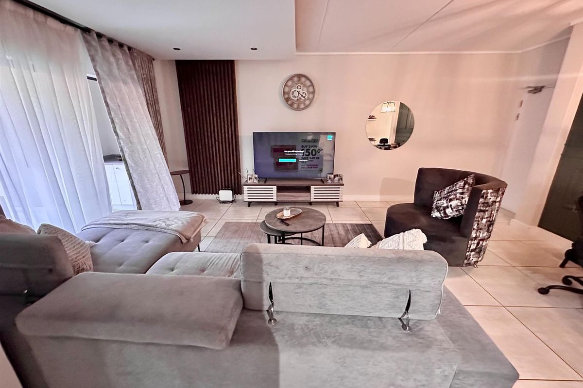 A well-maintained living room featuring tiled flooring, recessed ceiling lighting, and a feature wall with vertical timber paneling.