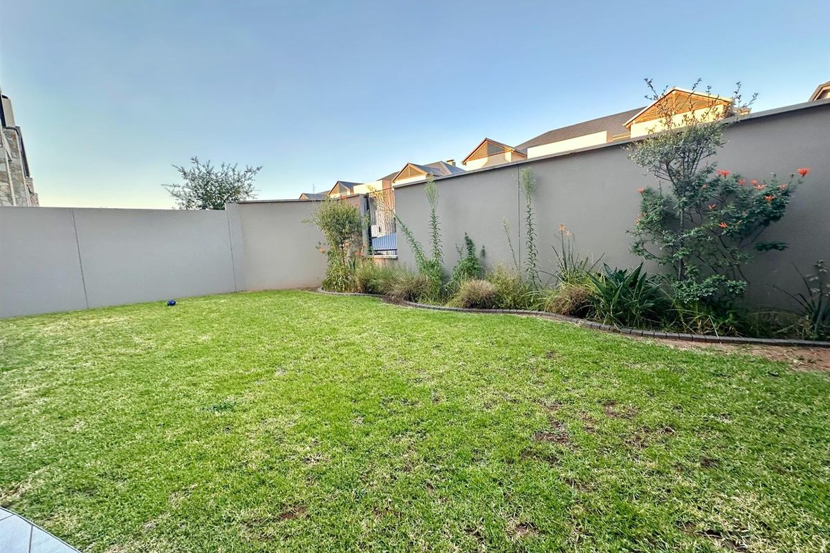 A private rear garden featuring a well-maintained lawn and perimeter boundary walls with established garden beds.