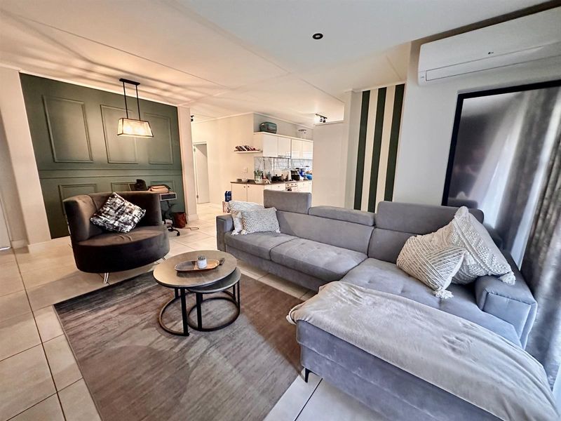 Open plan living area featuring tiled flooring, a decorative feature wall, and a wall-mounted air conditioning unit, flowing into the adjacent kitchen space.