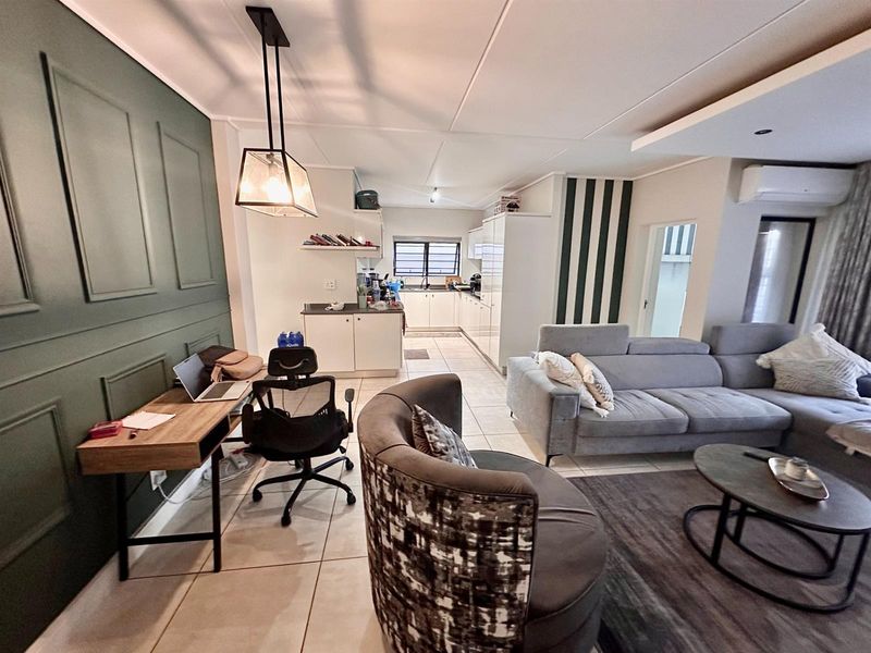 Open-plan living area featuring a modern kitchen with white cabinetry, tiled flooring, and a decorative accent wall in the lounge space.