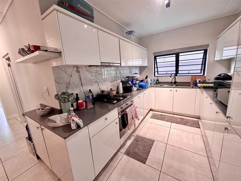 Modern kitchen featuring white high-gloss cabinetry, stone countertops, marble-look splashback, built-in oven, gas hob, and tiled flooring.