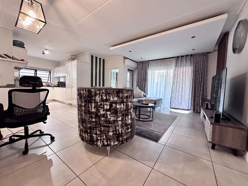 Open-plan living area featuring tiled flooring, recessed ceiling lighting, and a modern kitchen with white cabinetry, seamlessly flowing to a patio area.