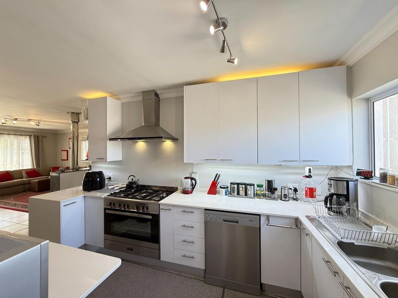 Modern open-plan kitchen featuring white cabinetry, quartz countertops, stainless steel gas stove, extractor fan, and integrated dishwasher, flowing into the adjacent living area.