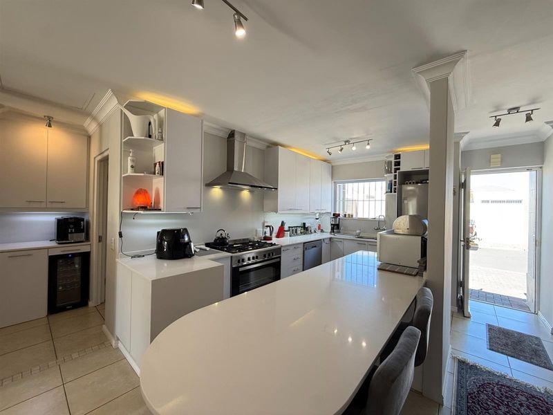 Modern kitchen featuring white cabinetry, quartz countertops with breakfast bar, gas stove, stainless steel extractor, and integrated lighting, leading to an exterior entrance.