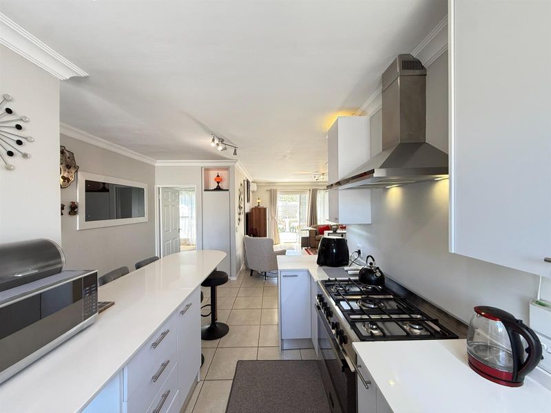 Modern open-plan kitchen featuring white cabinetry, quartz countertops, and a gas hob, flowing seamlessly into the living area with tiled flooring throughout.