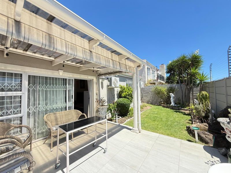 A covered patio area with tiled flooring, sliding door access, and an adjacent garden space featuring a boundary wall with electric fencing.