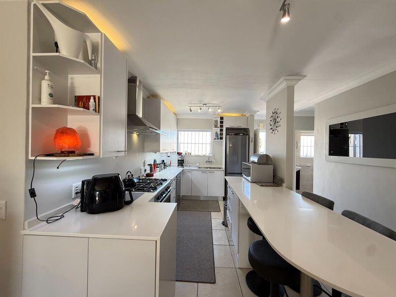 Modern kitchen featuring white cabinetry, quartz countertops, a gas hob, integrated breakfast bar, and recessed lighting, offering a clean and functional workspace.