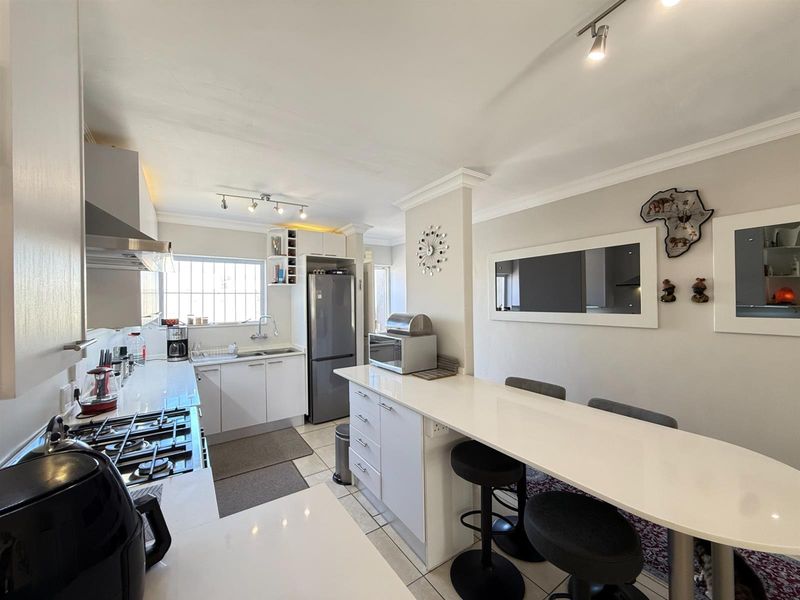 A modern, well-lit kitchen featuring white cabinetry, stone countertops, a gas hob with extractor, and an integrated breakfast bar for casual dining.