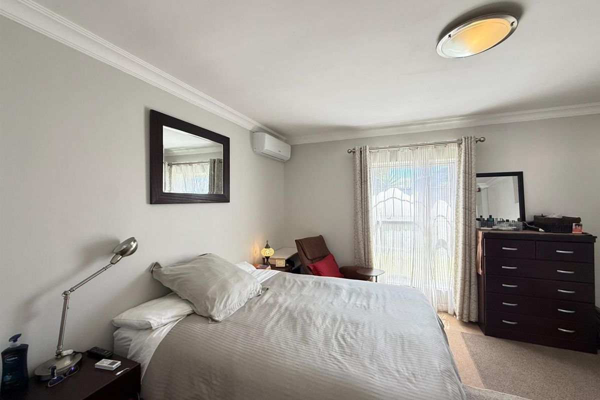A well-maintained bedroom featuring neutral walls, carpeted flooring, a wall-mounted air conditioning unit, and a sliding glass door providing natural light.