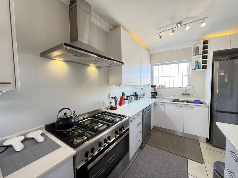 Modern kitchen featuring white cabinetry, stone countertops, a gas stove with extractor fan, and integrated storage solutions.