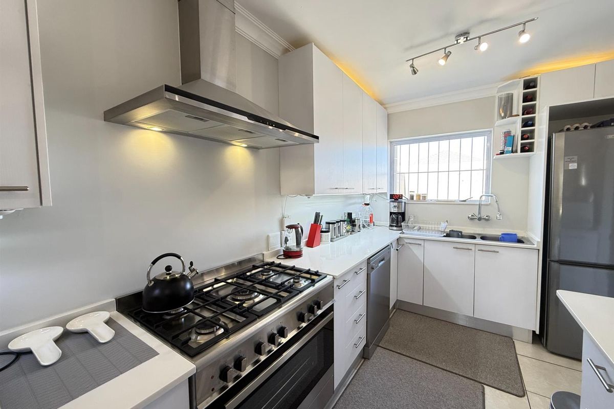 Modern kitchen featuring white cabinetry, stone countertops, a gas stove with extractor fan, and integrated storage solutions.