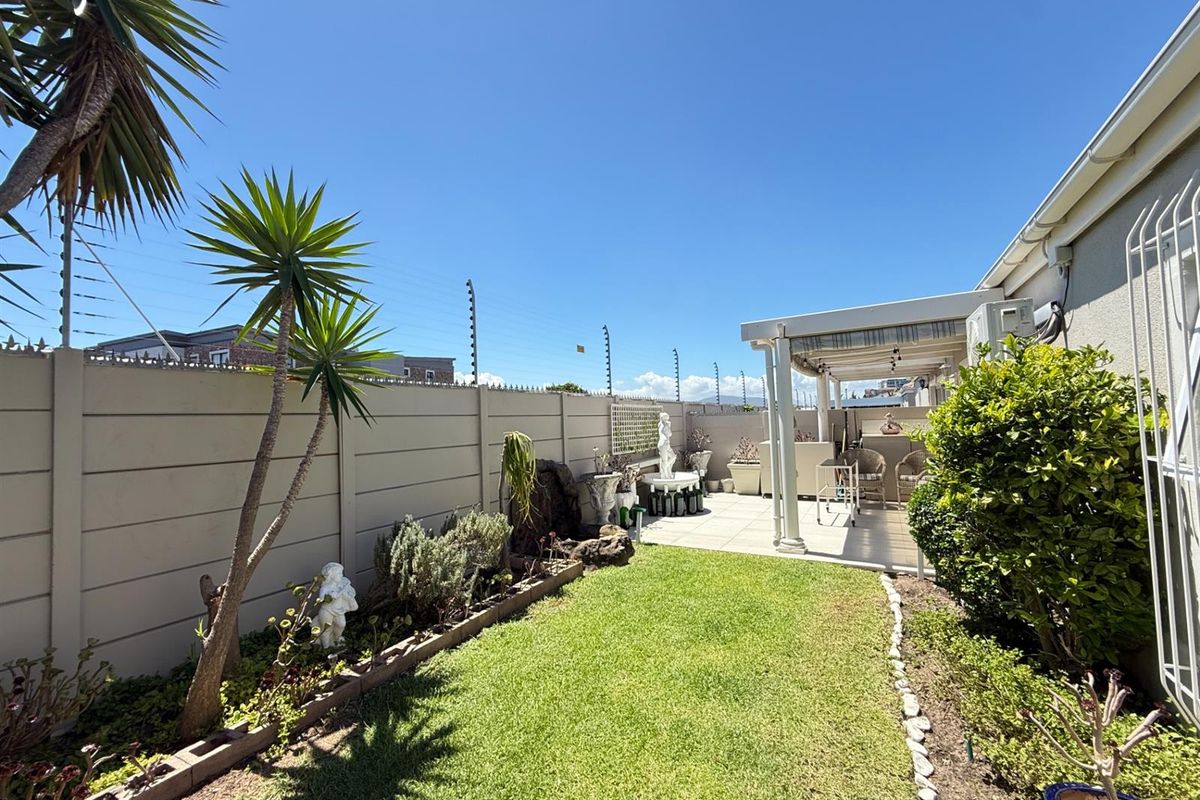 A well-maintained rear garden featuring a lawn, landscaped borders, and a covered patio area enclosed by secure electric fencing.