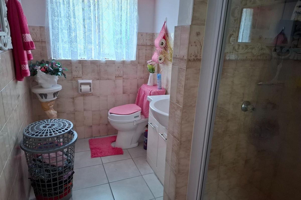 A functional bathroom featuring a shower enclosure, vanity basin, and toilet, finished with neutral wall tiles and floor tiling.
