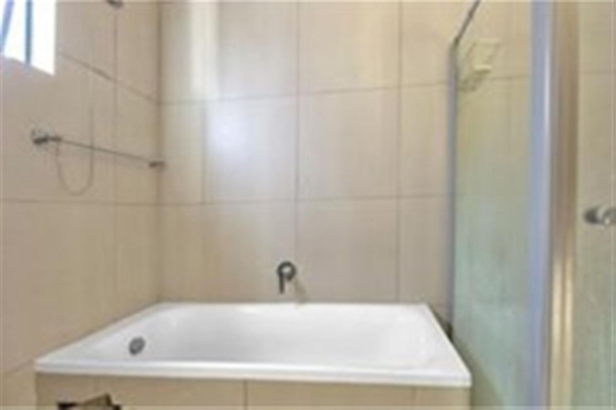 A functional bathroom featuring a built-in bathtub with wall-mounted faucet and a separate glass-enclosed shower stall with neutral wall tiling.