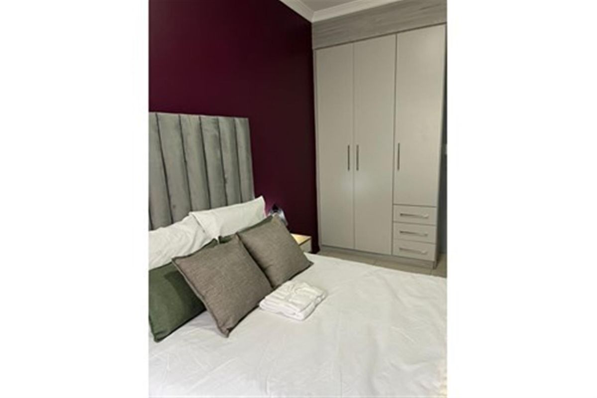 A well-maintained bedroom featuring a built-in wardrobe with integrated drawers and a decorative accent wall.