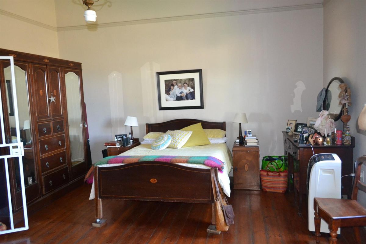 A spacious bedroom featuring original polished timber flooring and high ceilings, offering a classic aesthetic with potential for cosmetic updates.