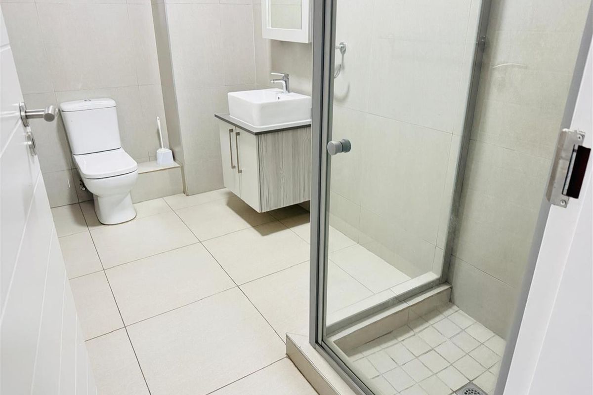 Modern bathroom featuring a glass-enclosed shower, a contemporary vanity with a vessel sink, and a white toilet with neutral floor and wall tiling.