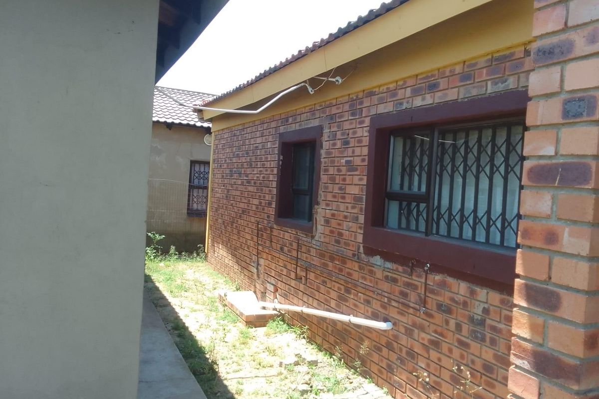 Side exterior view of the house featuring face brick walls, security bars on windows, and exposed external utility piping.