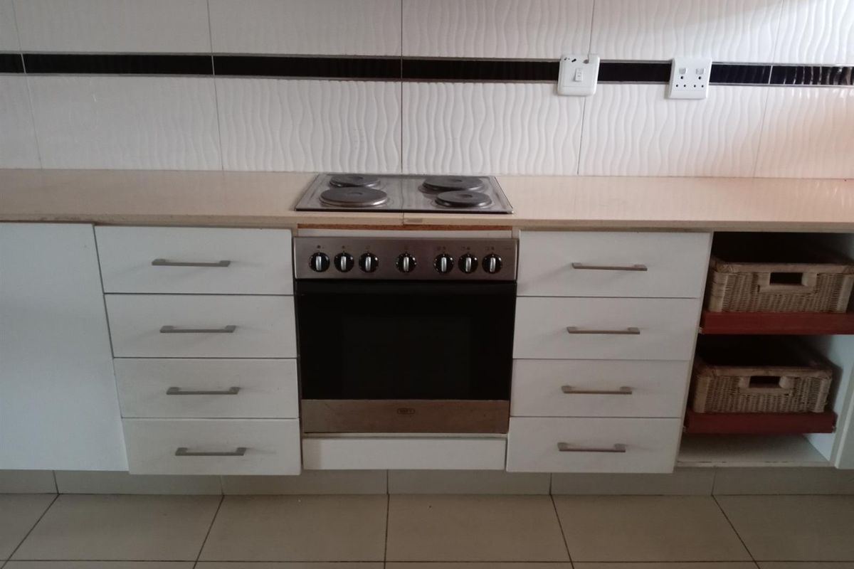 A functional kitchen workspace featuring a built-in electric oven and hob, tiled splashback, and white cabinetry with ample drawer storage.