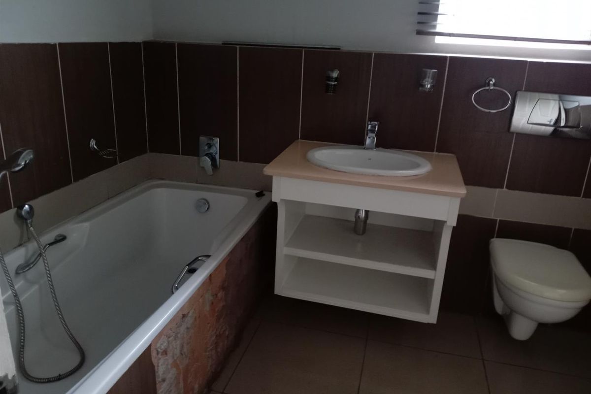 Bathroom featuring a bathtub with handheld shower, wall-mounted vanity with basin, and a wall-hung toilet with dark tiled walls.