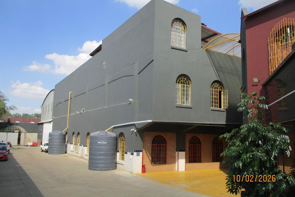 Exterior view of a multi-story commercial building featuring grey painted facade, arched windows, and external water storage tanks.