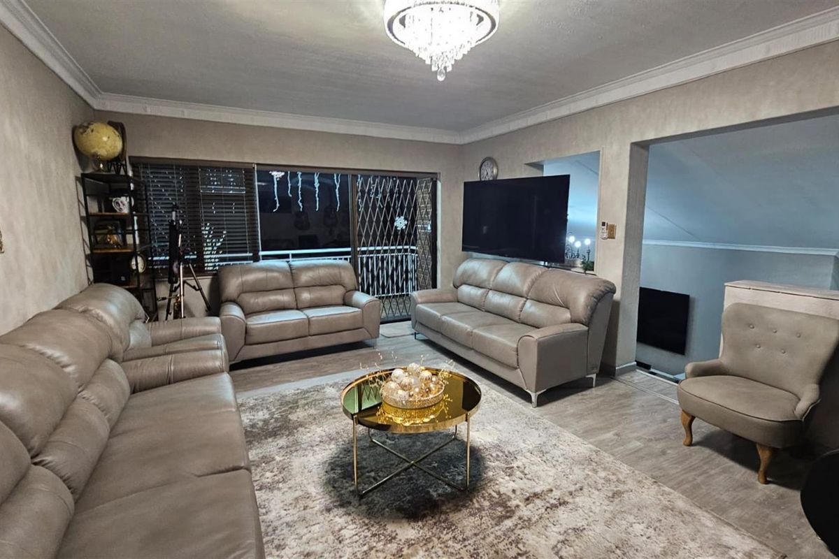 Spacious living room featuring neutral wall finishes, crown molding, and large sliding glass doors with security gates leading to an outdoor area.
