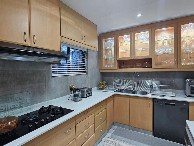 A functional kitchen featuring light wood cabinetry, stone countertops, a built-in gas hob, extractor fan, and integrated dishwasher space.
