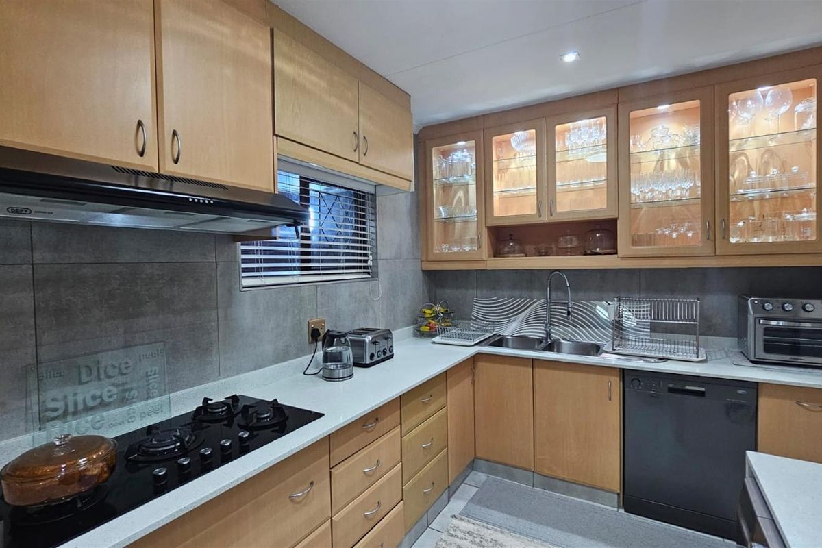 A functional kitchen featuring light wood cabinetry, stone countertops, a built-in gas hob, extractor fan, and integrated dishwasher space.