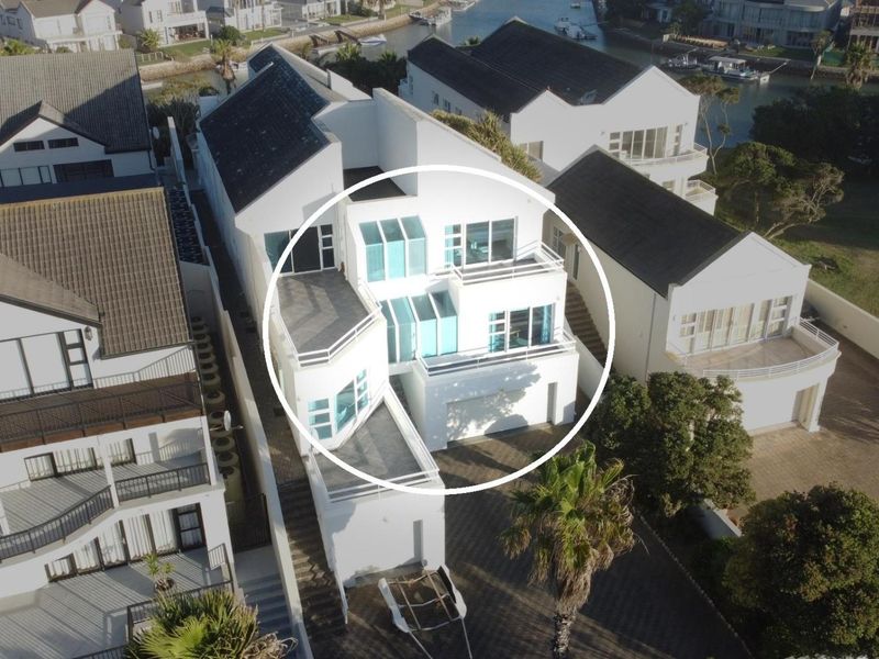 Aerial view of a modern multi-level residential property featuring multiple balconies, large windows, and a white facade in a waterfront estate setting.