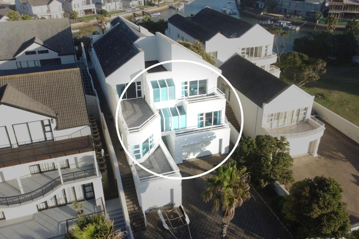 Aerial view of a modern multi-level residential property featuring multiple balconies, large windows, and a white facade in a waterfront estate setting.